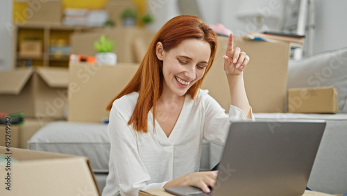 Young redhead woman using laptop sitting on floor at new home