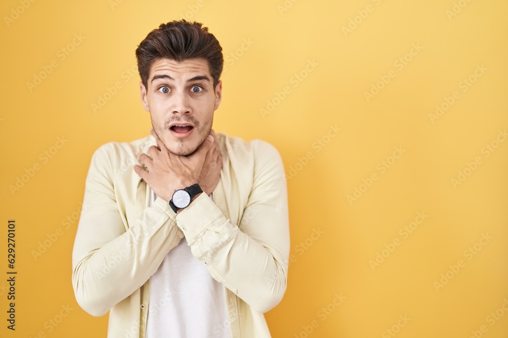 Young hispanic man standing over yellow background shouting suffocate because painful strangle. health problem. asphyxiate and suicide concept. Young hispanic man standing over yellow background shouting suffocate because painful strangle. health problem. asphyxiate and suicide concept.