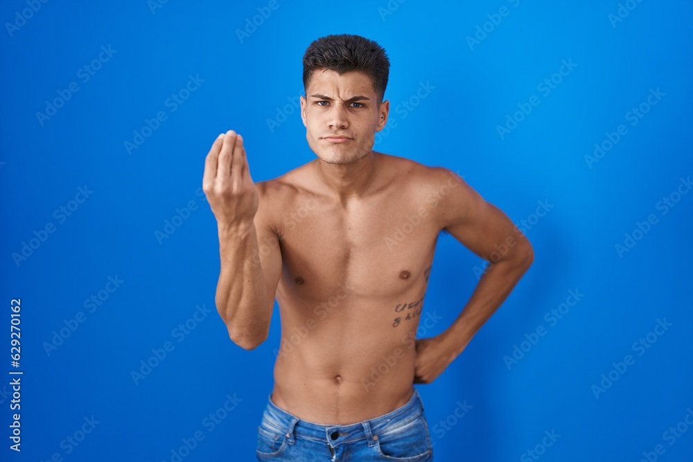Young hispanic man standing shirtless over blue background doing italian gesture with hand and fingers confident expression