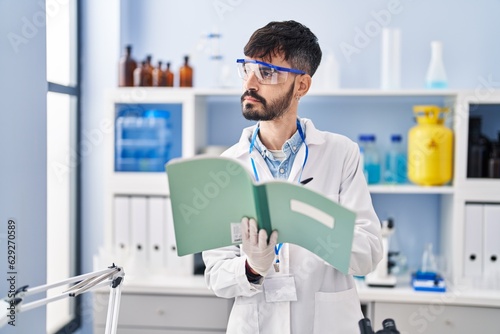 Young hispanic man scientist writing on notebook working at laboratory
