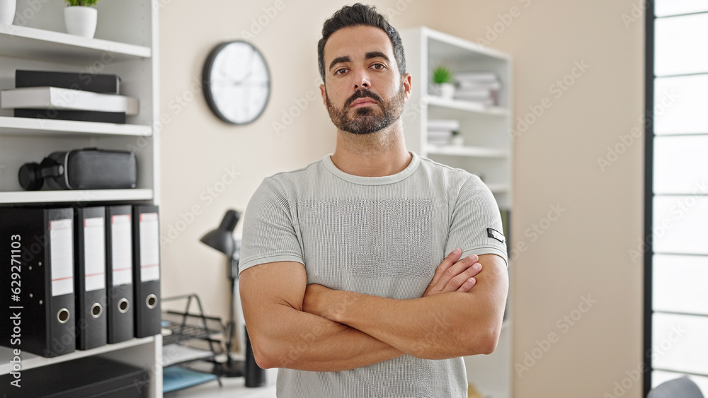 Young hispanic man business worker standing with arms crossed gesture at office