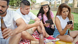 Group of people having picnic using smartphones and touchpad at park