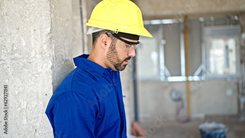 Young hispanic man worker leaning on wall tired at construction site