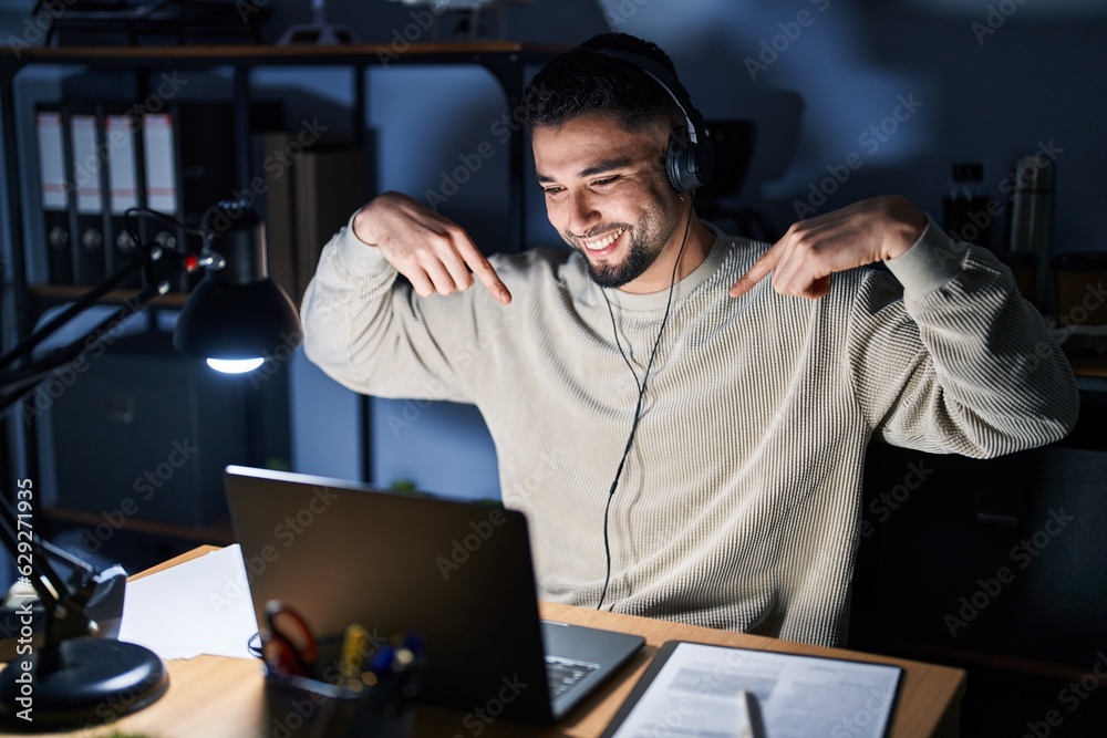 Young handsome man working using computer laptop at night looking confident with smile on face, pointing oneself with fingers proud and happy.