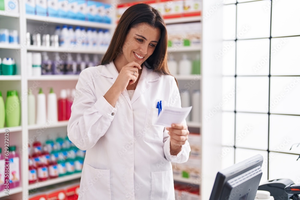 Young beautiful hispanic woman pharmacist smiling confident reading prescription at pharmacy