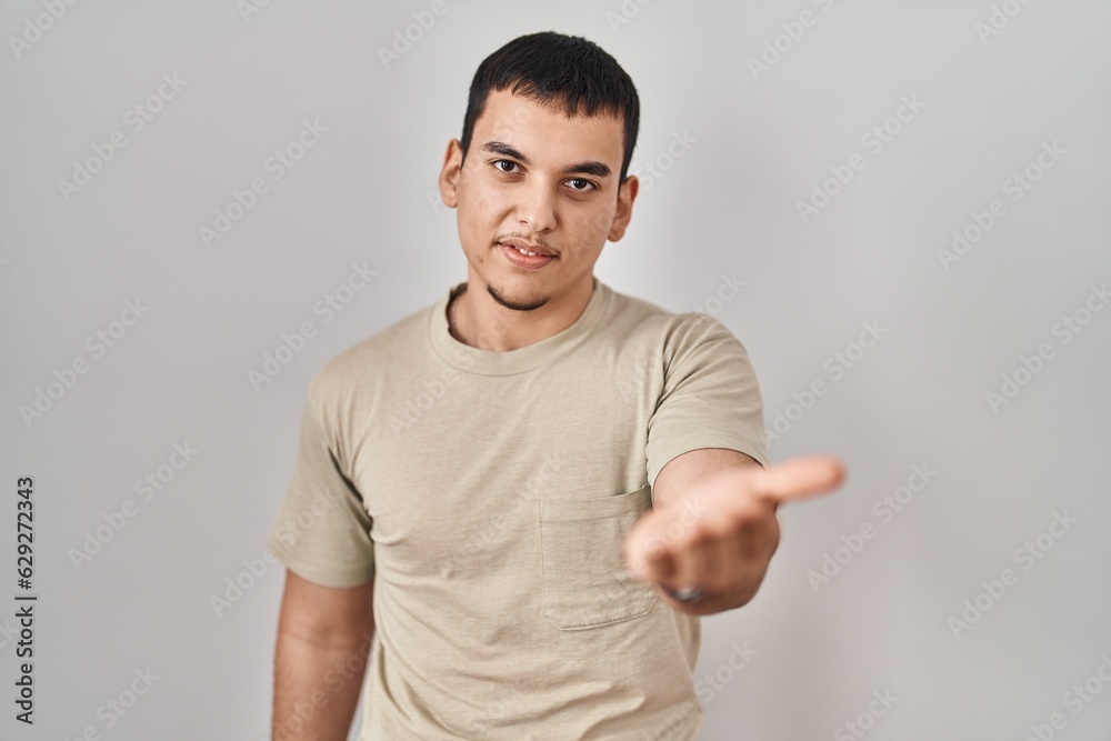 Young arab man wearing casual t shirt smiling cheerful offering palm hand giving assistance and acceptance. Young arab man wearing casual t shirt smiling cheerful offering palm hand giving assistance and acceptance.