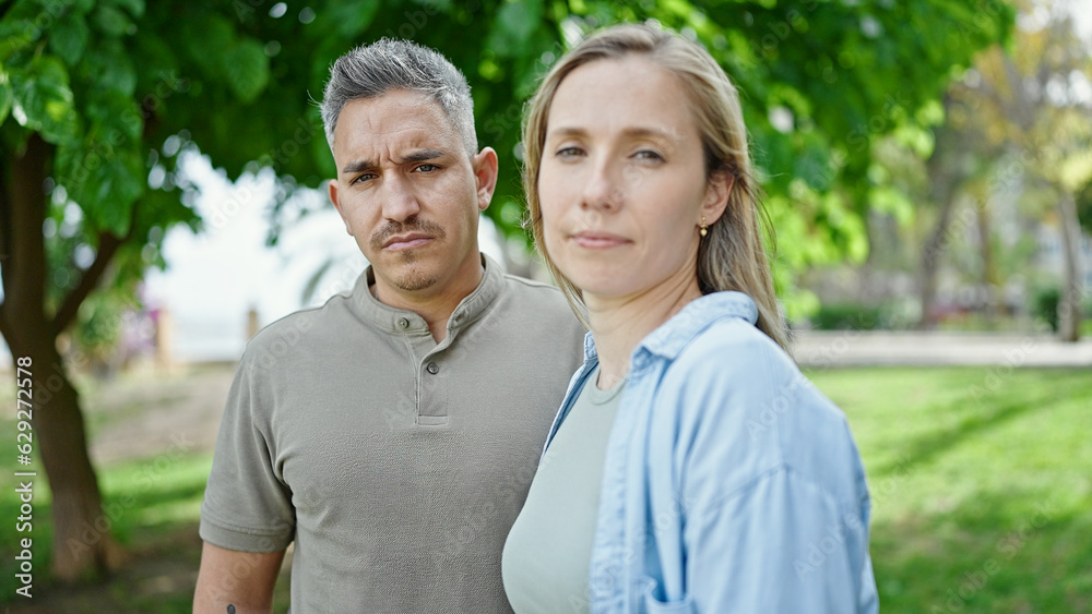 Man and woman couple standing together with serious face at park Man and woman couple standing together with serious face at park