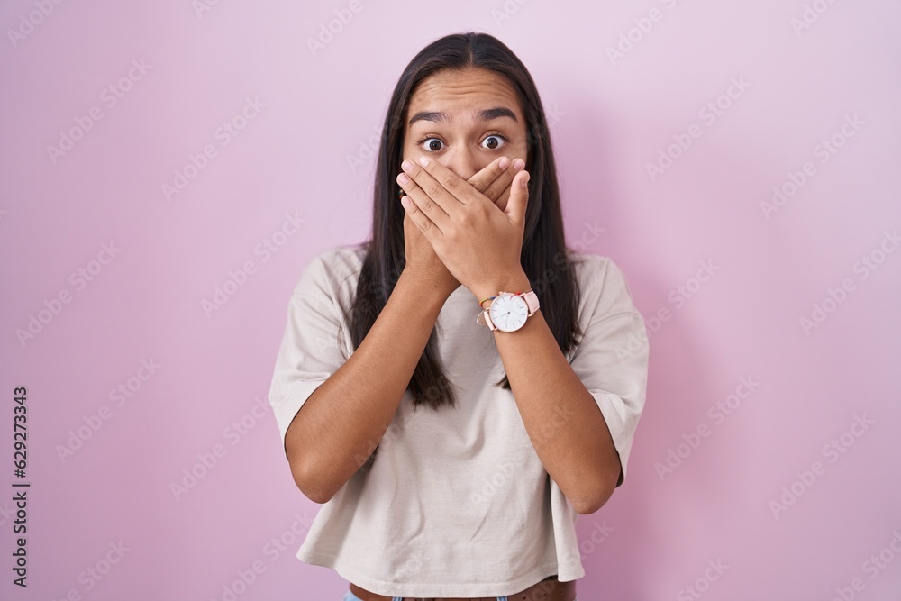 Young hispanic woman standing over pink background shocked covering mouth with hands for mistake. secret concept. Young hispanic woman standing over pink background shocked covering mouth with hands for mistake. secret concept.