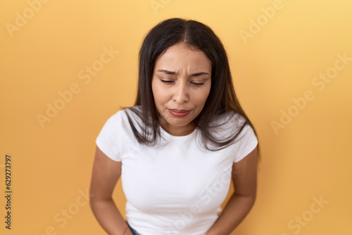 Young arab woman wearing casual white t shirt over yellow background with hand on stomach because indigestion, painful illness feeling unwell. ache concept. © Krakenimages.com