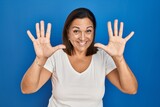 Hispanic mature woman standing over blue background showing and pointing up with fingers number ten while smiling confident and happy.