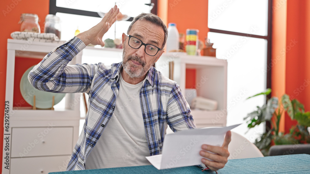 Fototapeta premium Middle age man angry reading document sitting on table at dinning room