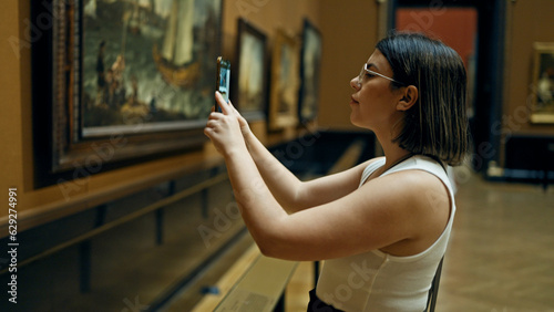 Young beautiful hispanic woman visiting art gallery taking pictures with smartphone at Art Museum in Vienna