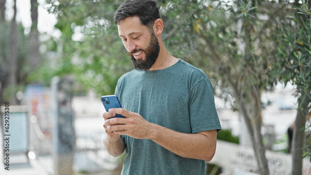 Fototapeta premium Young hispanic man using smartphone smiling at park