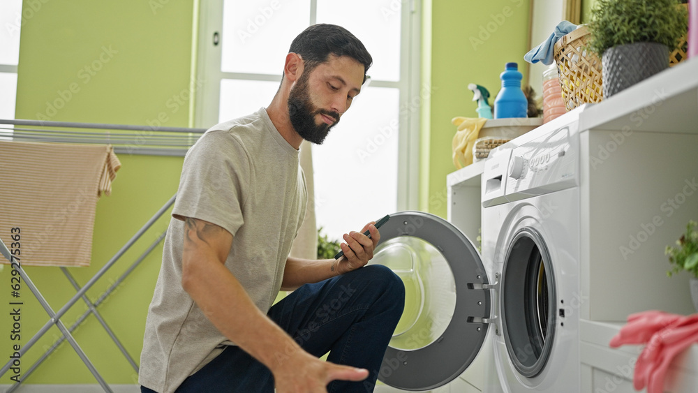 Obraz premium Young hispanic man washing clothes at laundry room