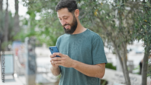 Young hispanic man using smartphone smiling at park