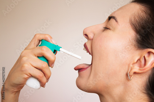 a young caucasian dark - haired woman suffers from a viral or colds disease, sprays a sore throat spray into her mouth close-up. the concept of health.