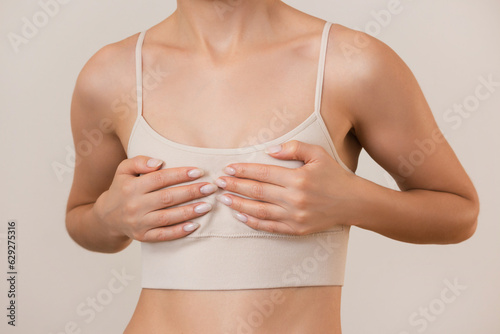 a young woman in beige underwear holds her small breasts with both hands isolated on a beige background. Women's Health