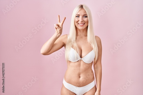 Caucasian woman wearing lingerie over pink background showing and pointing up with fingers number two while smiling confident and happy.