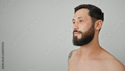 Young hispanic man standing shirtless looking to the side over isolated white background