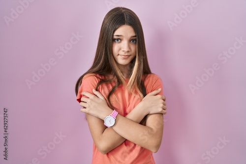 Teenager girl standing over pink background shaking and freezing for winter cold with sad and shock expression on face