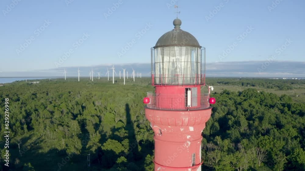 This is a Light house in the North of Europe on the Baltic Sea during summer, the landscape and is beautiful. Behind the lighthouse are a forest and after that few wind generator.
