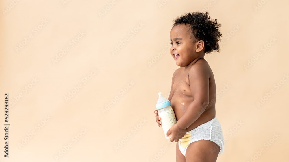 Φωτογραφία A 2-year-old Nigerian baby girl with beautiful curly hair, standing and holding milk bottle, happy and smile, on light brown background