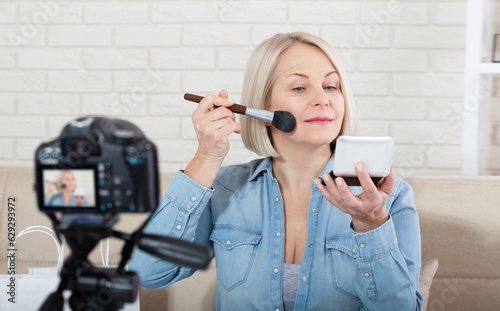 Woman doing makeup demonstrating cosmetics and shooting herself on video camera at home