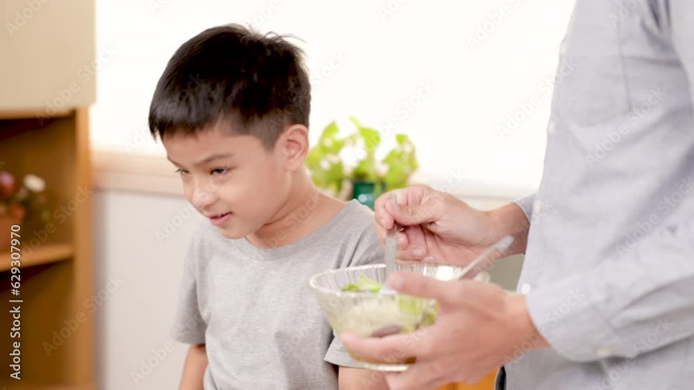 family activities lifestyles in kitchen, upset Asian kids dislike vegetables bad smell feeling, father try to encourage son to eat vegetable tomatoes in kitchen, unhappy kids disgusting salad in bowl family activities lifestyles in kitchen, upset Asian kids dislike vegetables bad smell feeling, father try to encourage son to eat vegetable tomatoes in kitchen, unhappy kids disgusting salad in bowl