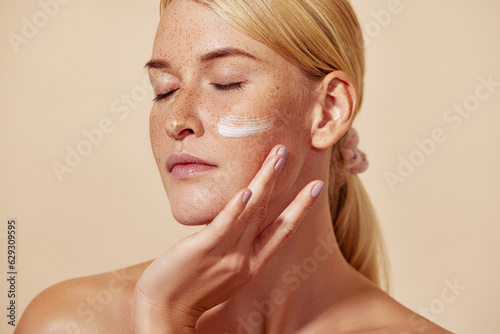 Beautiful young female with closed eyes applying white cream on her face