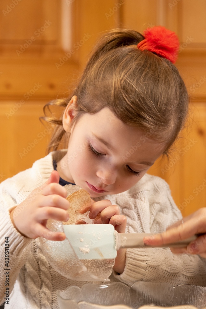Little girl concentrated baking a gingerbread house on a school holiday with her family helping her in the kitchen. Little girl concentrated baking a gingerbread house on a school holiday with her family helping her in the kitchen.