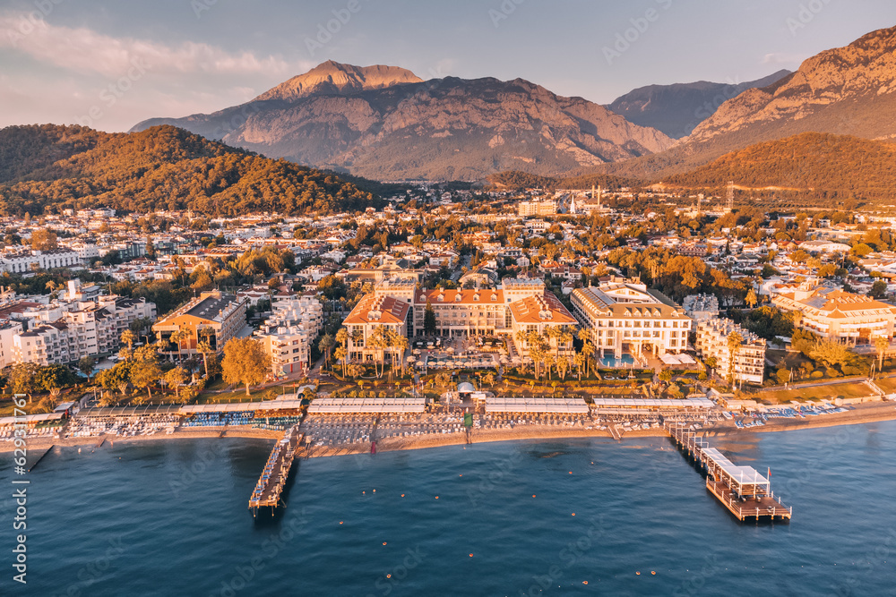 Fototapeta premium Discover a slice of paradise with striking aerial view, capturing the perfect blend of relaxation and natural wonder in Kemer, featuring hotels, a serene sea beach, and majestic mountains.