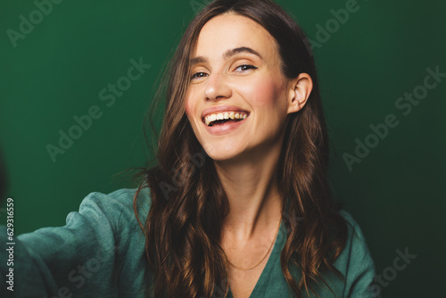 Fotografija Portrait of young happy brunette curly hair woman with toothy smile laughing isolated over green wall background make selfie looking camera
