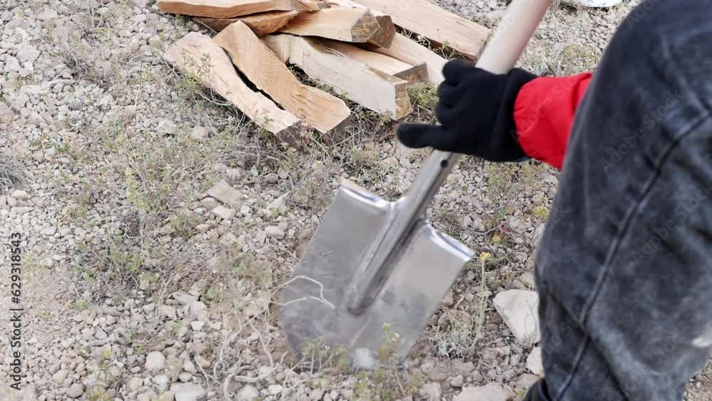 A teenage hiker uses a sharp camping shovel to dig a fire pit in rocky