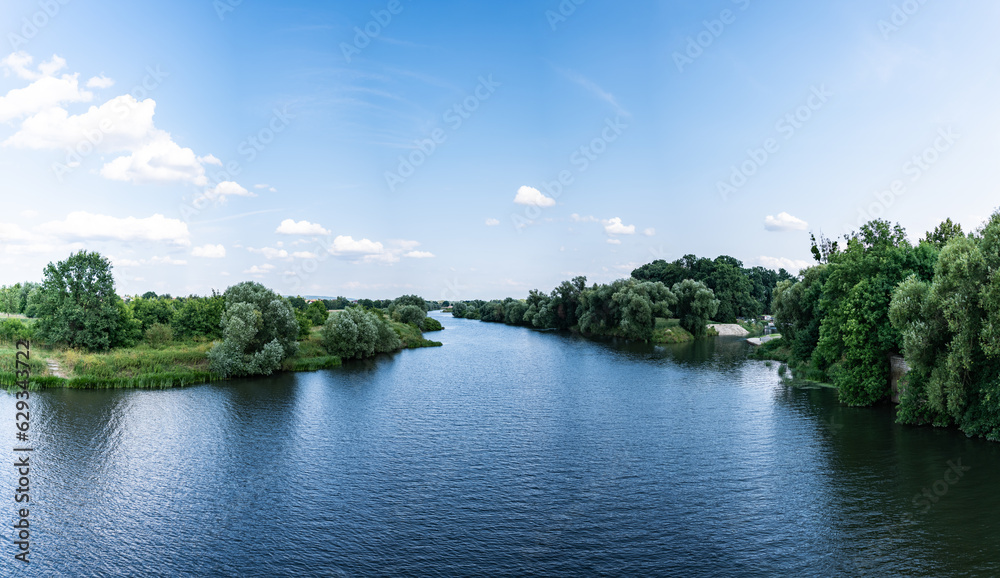 Panorama rzeki Odry w tle lekko pochmurna pogoda, błękit nieba zieleń przy brzegu, pora letnia, Odra w odcinku województwa Opolskiego - obrazy, fototapety, plakaty 