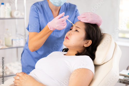 Professional cosmetologist injecting the medication under patient skin in procedure cabinet
