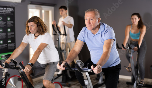 Portrait of active elderly man doing cardio training, cycling on stationary bike in gym ..