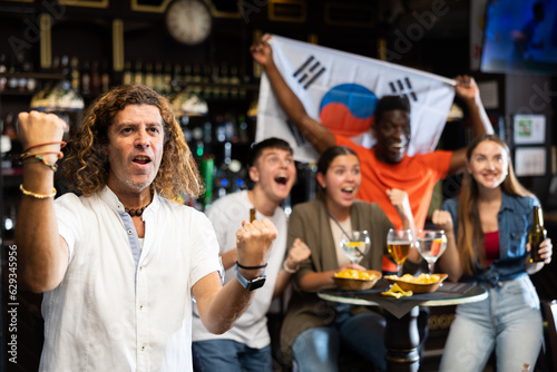 Group of happy fans celebrate victory of their favorite team with flag of South Korea in a beer bar