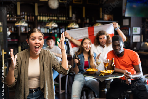 Surprised caucasian woman, fan of England team, scraming chants while watching sport competition in bar with her friends.