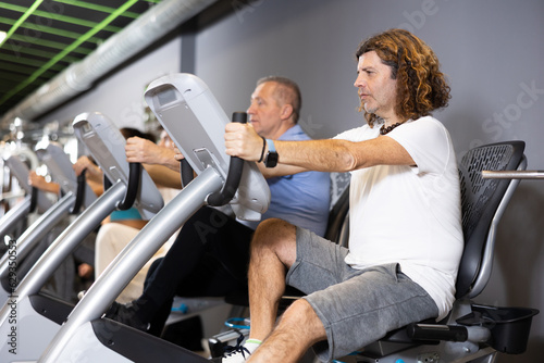 Portrait of concentrated adult man doing cardio training, cycling on stationary bike in gym. Sport and fitness concept