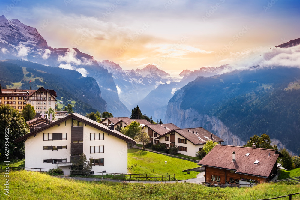 Wengen town in Switzerland at sunset. View over Swiss Alps near Lauterbrunnen valley. Typical Swiss houses in Wengen. Mountain peaks of Eiger and Jungfrau covered with snow and clouds