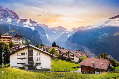 Wengen town in Switzerland at sunset. View over Swiss Alps near Lauterbrunnen valley. Typical Swiss houses in Wengen. Mountain peaks of Eiger and Jungfrau covered with snow and clouds © Julia Lavrinenko