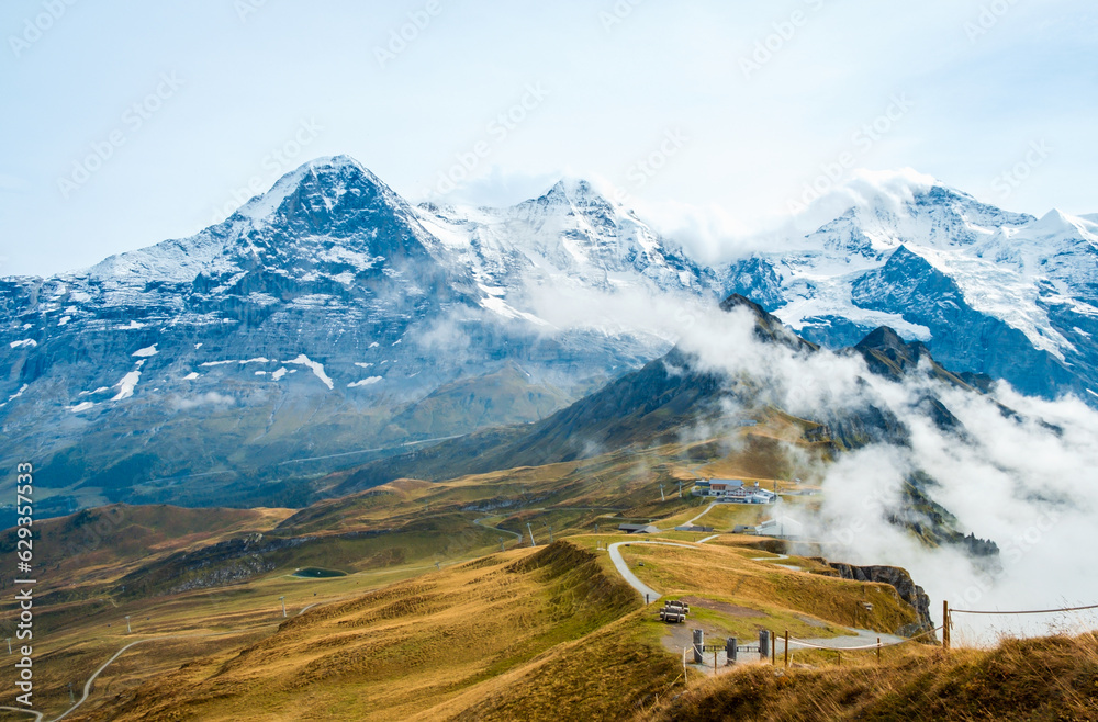 Autumn in Swiss Alps. Hiking trail on top of Mannlichen near Wengen and Lauterbrunnen, Switzerland. Mountain range with peaks Eiger, Monch, Jungfraujoch and Jungfrau in low clouds