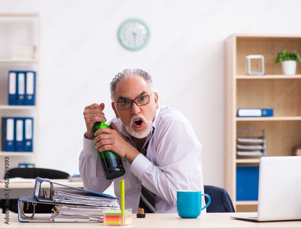Old male employee drinking alcohol in the office Old male employee drinking alcohol in the office