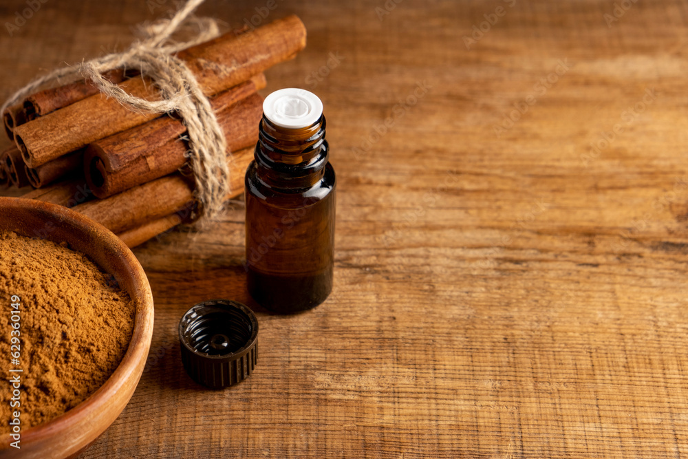 Essential cinnamon oil in a small bottle, ground cinnamon and cinnamon sticks on old wooden background.