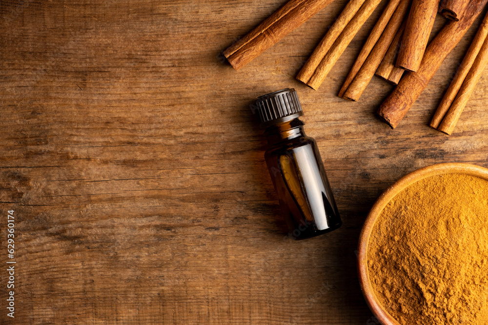 Essential cinnamon oil in a small bottle, ground cinnamon and cinnamon sticks on old wooden background.