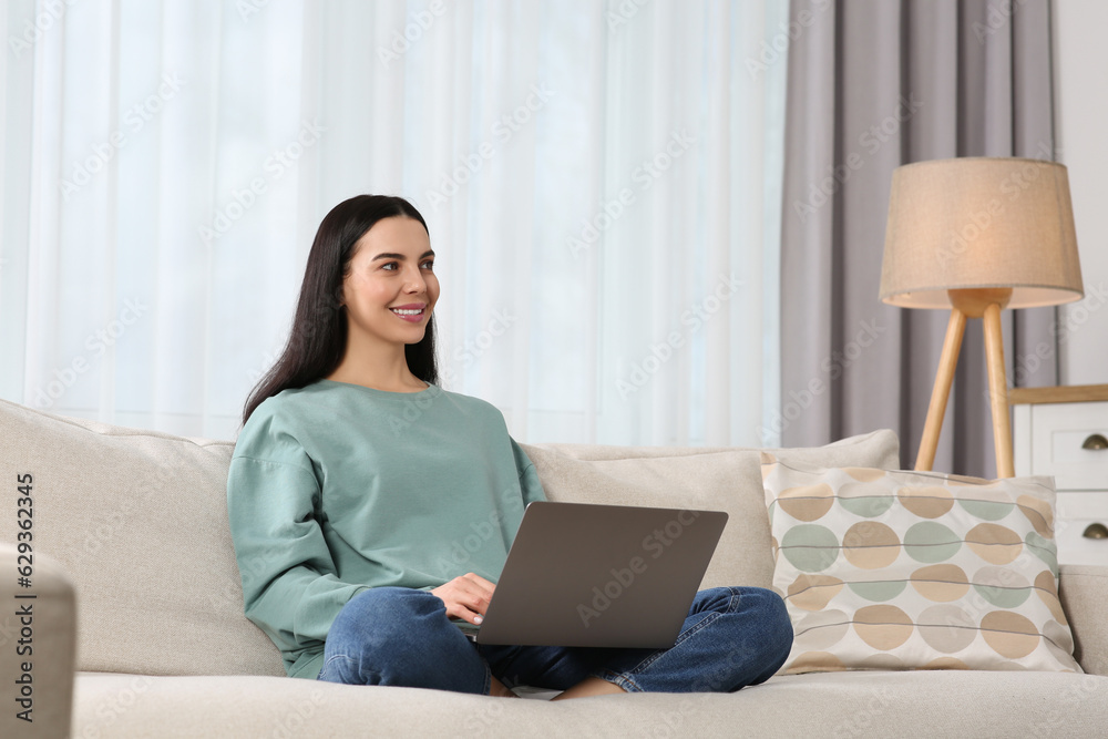 Fototapeta premium Happy woman working with laptop on sofa at home