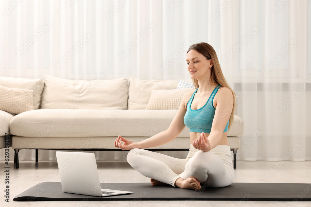 Woman in sportswear meditating near laptop at home. Harmony and zen Woman in sportswear meditating near laptop at home. Harmony and zen