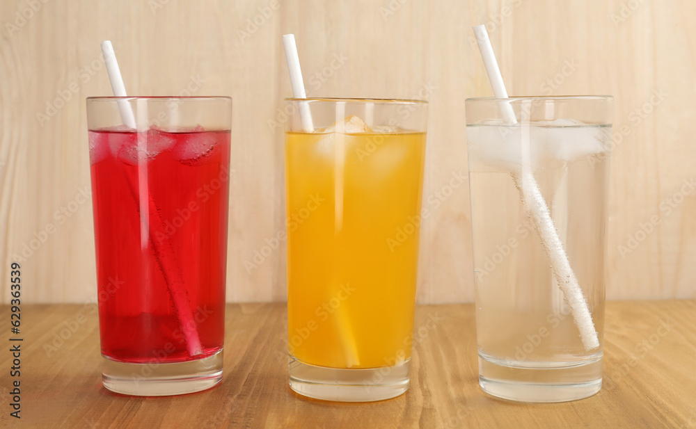 Glasses of different refreshing soda water with ice cubes and straws on wooden table Glasses of different refreshing soda water with ice cubes and straws on wooden table