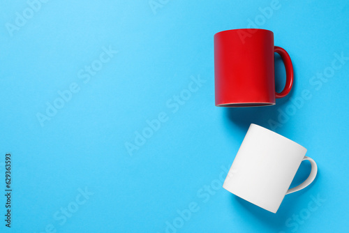 White and red ceramic mugs on light blue background, flat lay. Space for text