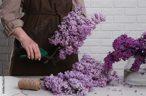 Woman trimming lilac branches with secateurs at white wooden table  closeup